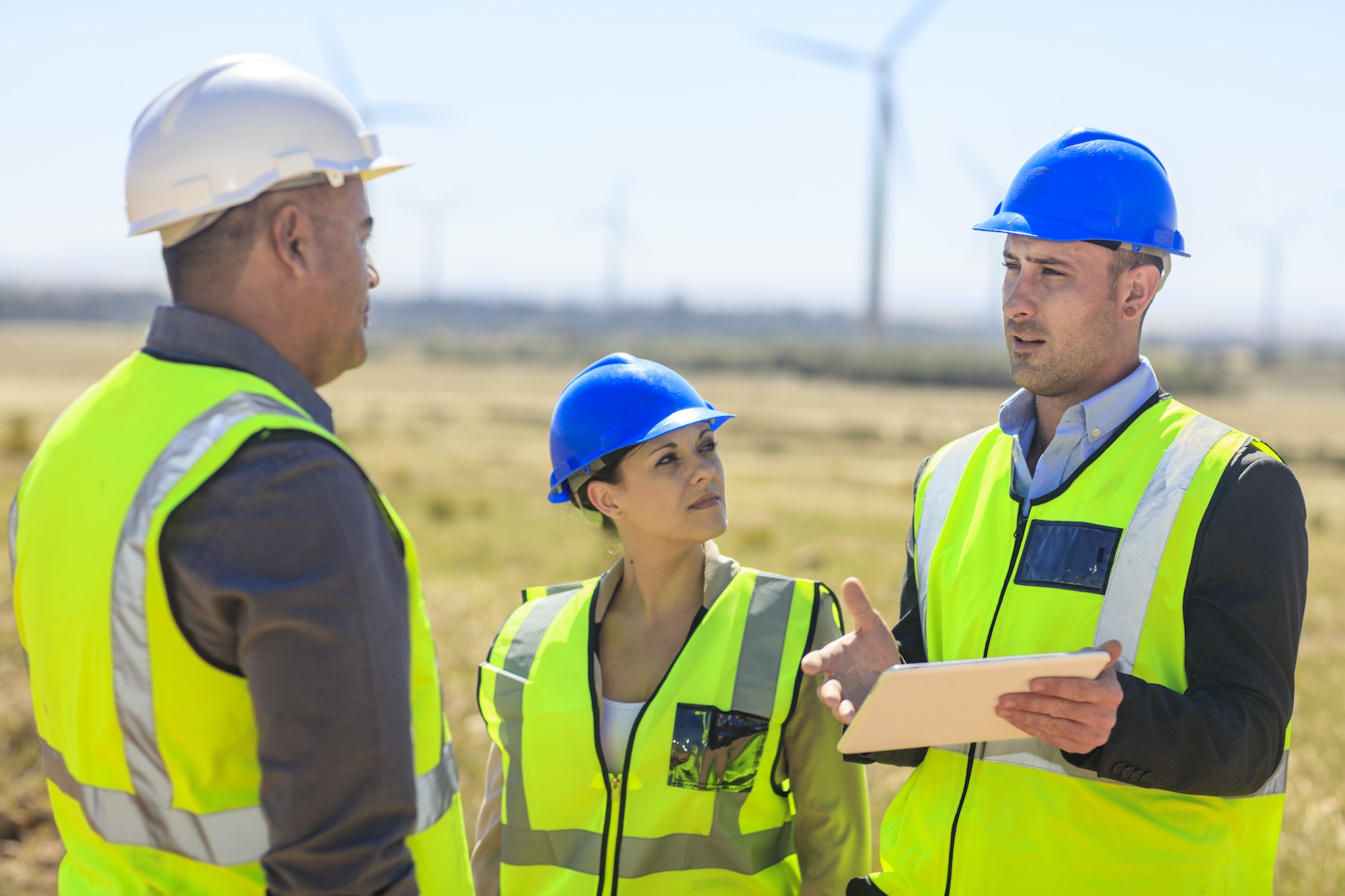 Three engineers with tablet discussing on a wind farm