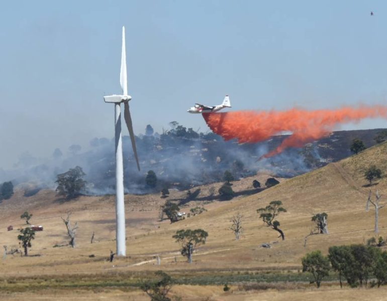 Aerial view of fire bombing plane flying dropping water near wind turbine