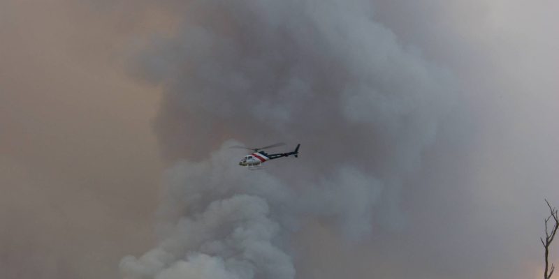 View of fire fighting helicopter flying through smoke